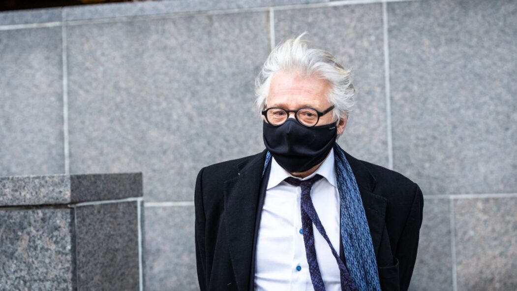 Gilbert Rozon portant un masque devant un mur du palais de justice de Montréal.